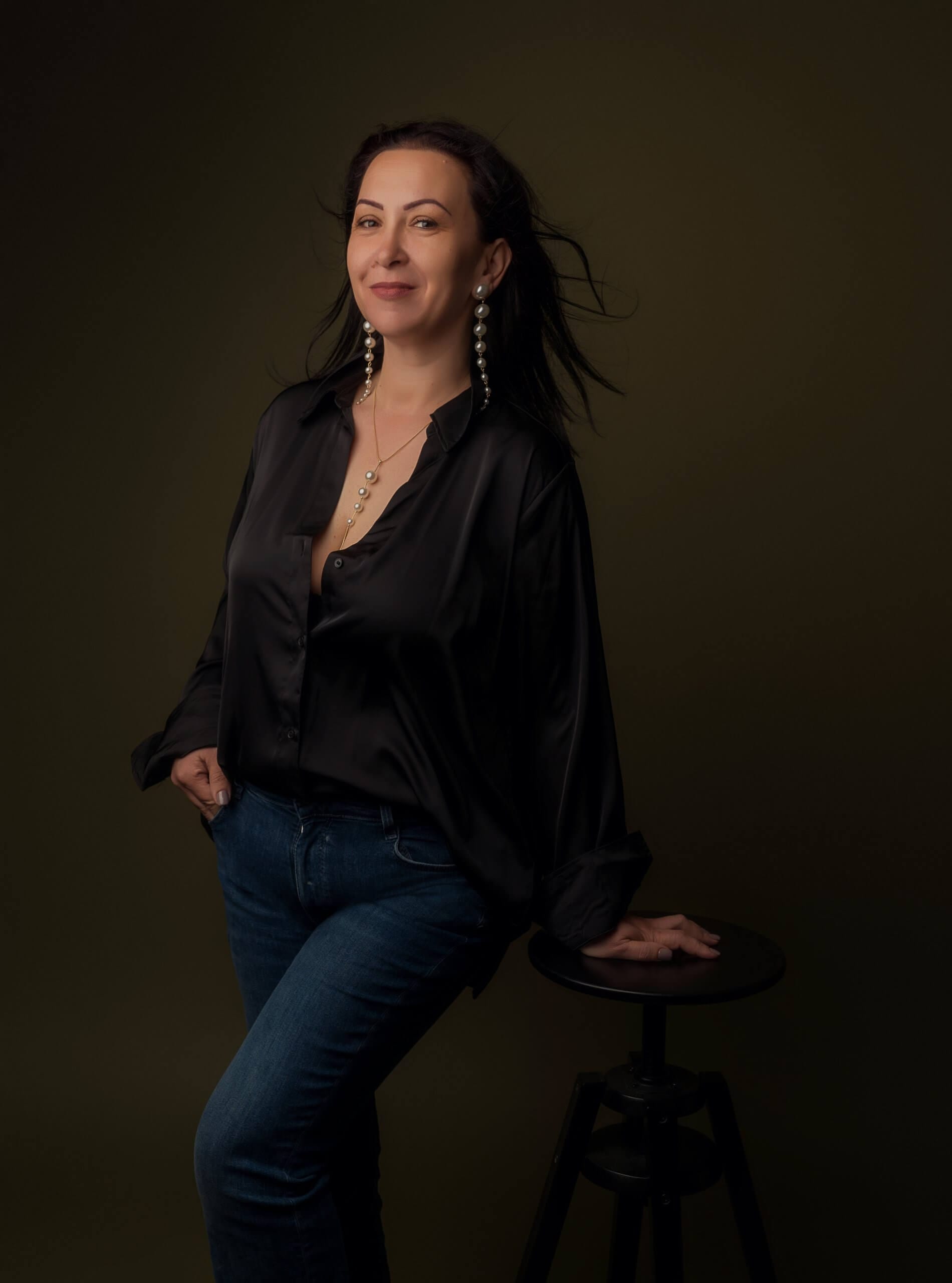 Femeie zâmbitoare în bluză neagră și blugi.